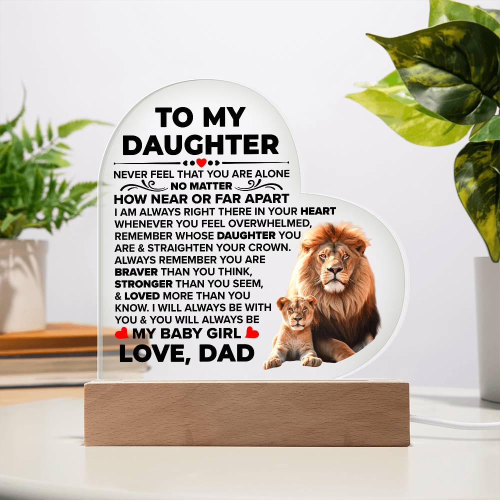 Daughter lion-and-cub heart plaque displayed on a wooden base beside houseplants in daylight.D